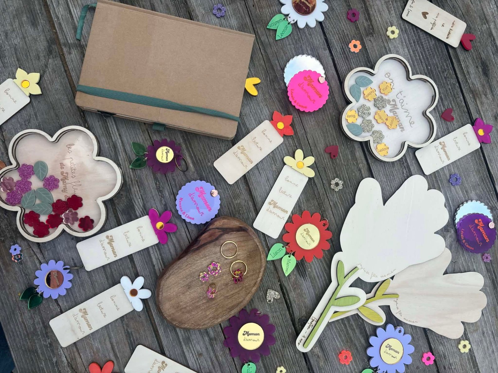 Créations AbracadaBois : marque-pages gravés, fleurs en plexiglas colorées et bijoux personnalisés posés sur une table en bois