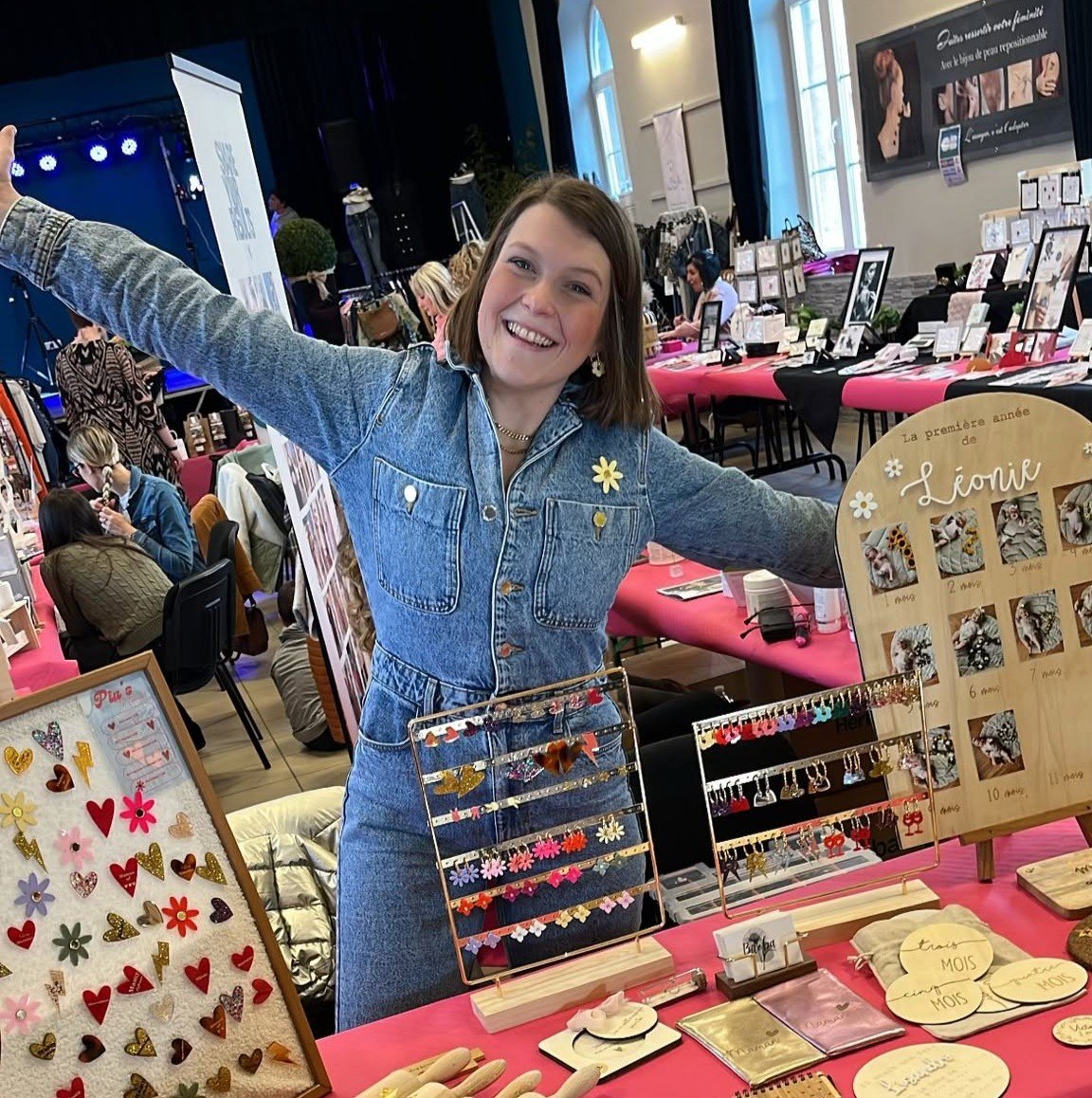 Morgane, souriante et les bras ouverts, derrière son stand AbracadaBois sur un marché de créateurs